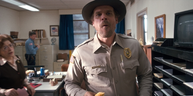 Medium shot frame from Stranger Things — sitting, book, standing