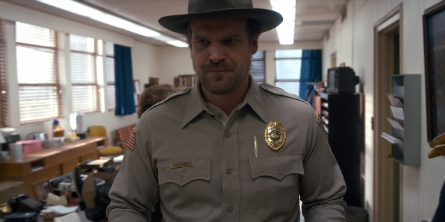 Wide shot frame from Stranger Things — standing, room, hat