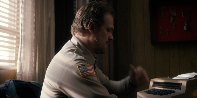 Wide shot frame from Stranger Things — sitting, shirt, office