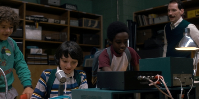 Wide shot frame from Stranger Things — standing, table, suit