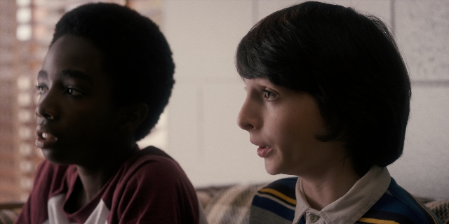 Wide shot frame from Stranger Things — sitting, room, shirt