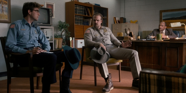 Wide shot frame from Stranger Things — sitting, room, table