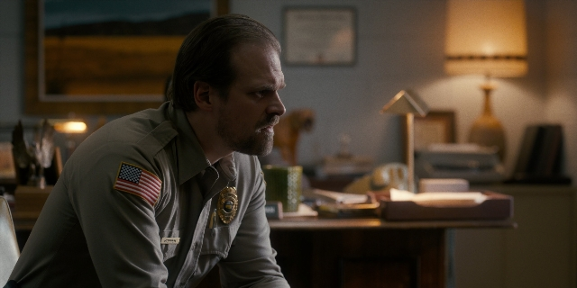 Wide shot frame from Stranger Things — sitting, room, table