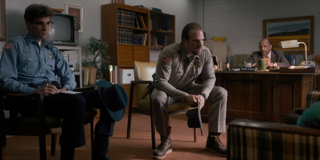 Wide shot frame from Stranger Things — sitting, room, table