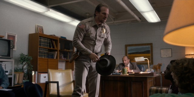Wide shot frame from Stranger Things — sitting, book, standing