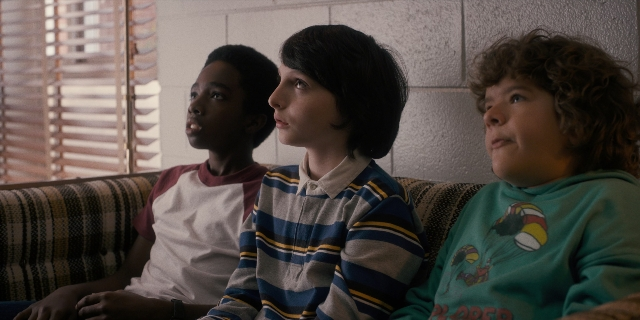 Wide shot frame from Stranger Things — sitting, room, shirt