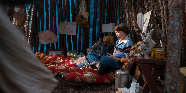 Wide shot frame from Stranger Things — sitting, book, bed