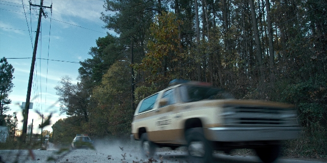 Wide shot frame from Stranger Things — plate, door, street
