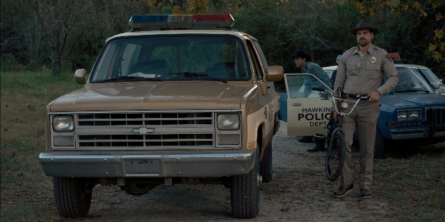 Wide shot frame from Stranger Things — standing, street, hat