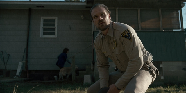 Wide shot frame from Stranger Things — walking, uniform, dog