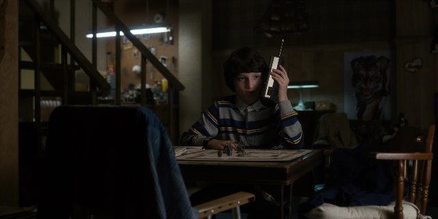 Wide shot frame from Stranger Things — sitting, room, table