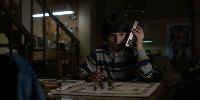 Wide shot frame from Stranger Things — sitting, room, table