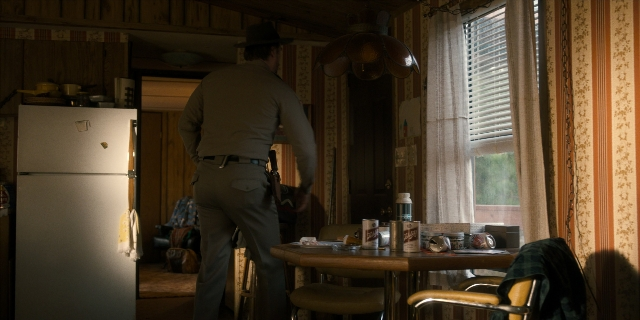 Wide shot frame from Stranger Things — standing, table, hat