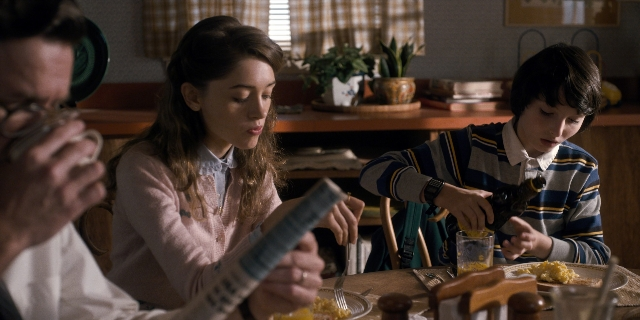 Wide shot frame from Stranger Things — sitting, book, table