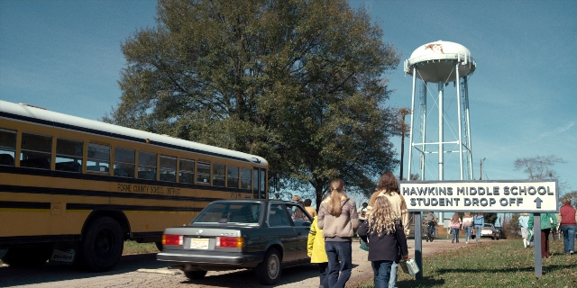 Wide shot frame from Stranger Things — walking, street, car