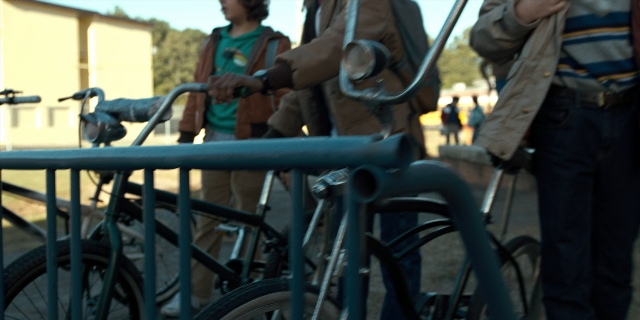 Wide shot frame from Stranger Things — standing, bicycle, shirt