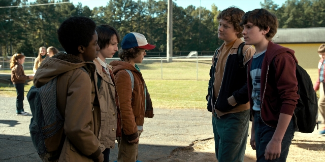Wide shot frame from Stranger Things — standing, street, hat