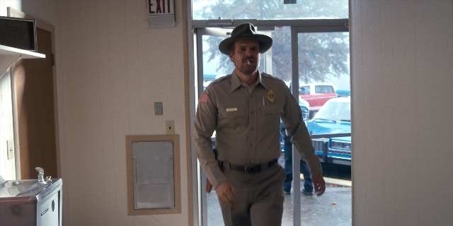 Wide shot frame from Stranger Things — standing, door, street
