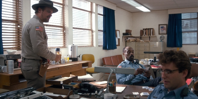 Wide shot frame from Stranger Things — sitting, desk, standing