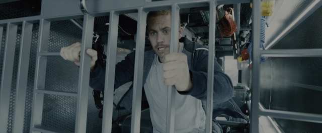 Wide shot frame from Fast & Furious 7 — sitting, room, hat