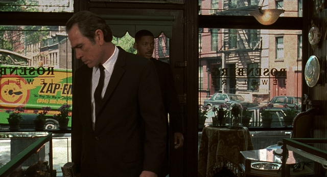 Wide shot frame from Men in Black — standing, table, phone
