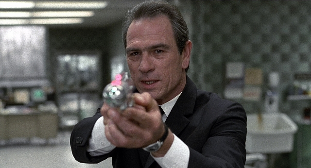 Medium shot frame from Men in Black — hand, suit, gun