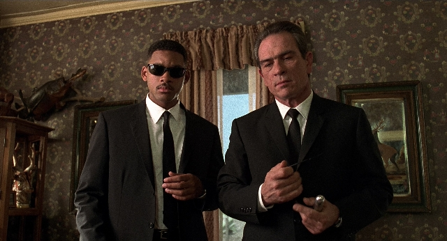 Wide shot frame from Men in Black — standing, room, hand