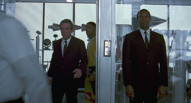 Wide shot frame from Men in Black — standing, room, door