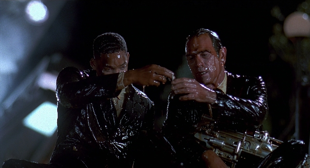 Wide shot frame from Men in Black — sitting, hand, face