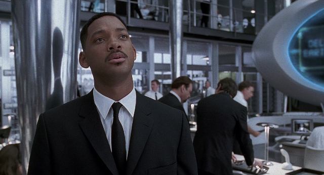 Wide shot frame from Men in Black — standing, room, suit