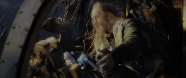 Wide shot frame from Mortal Engines — sitting, hat, coat