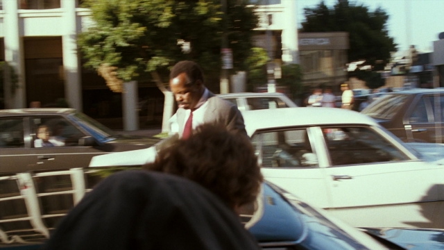 Wide shot frame from Lethal Weapon — walking, street, car