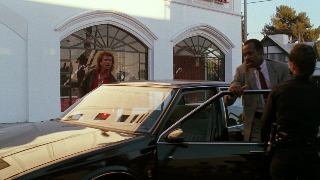 Wide shot frame from Lethal Weapon — standing, uniform, car