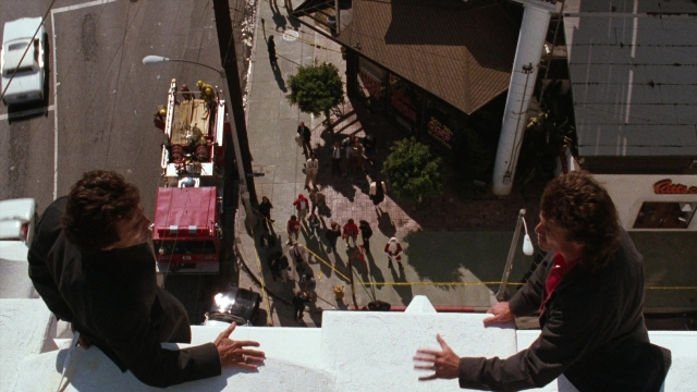 Wide shot frame from Lethal Weapon — sitting, dialogue, street