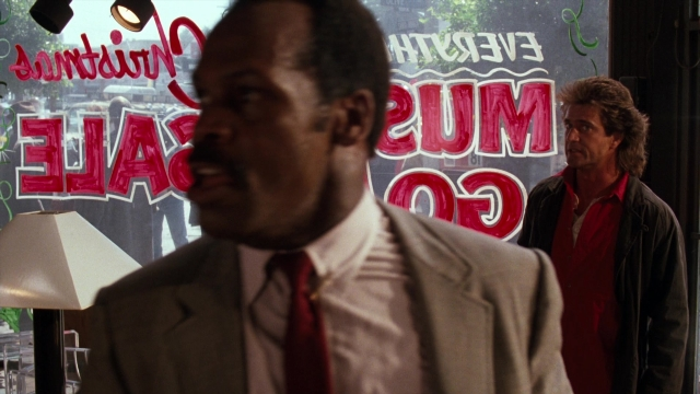 Wide shot frame from Lethal Weapon — standing, table, dialogue