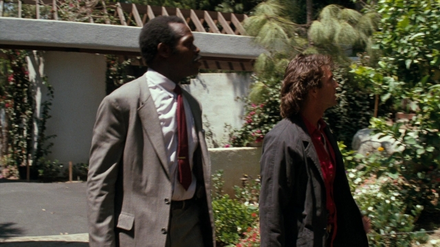 Wide shot frame from Lethal Weapon — standing, dialogue, suit