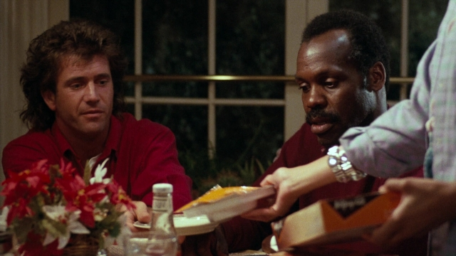Medium shot frame from Lethal Weapon — sitting, plate, table