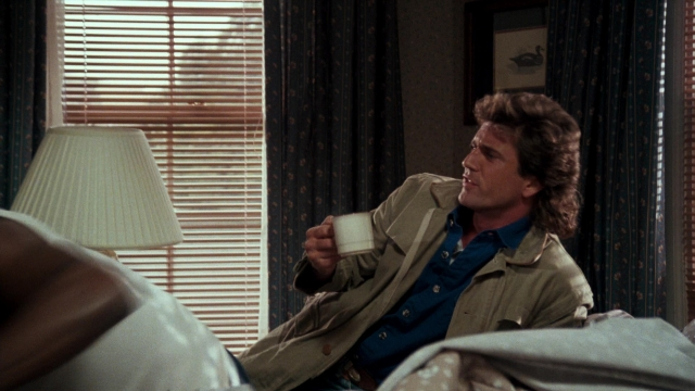 Wide shot frame from Lethal Weapon — sitting, room, coat