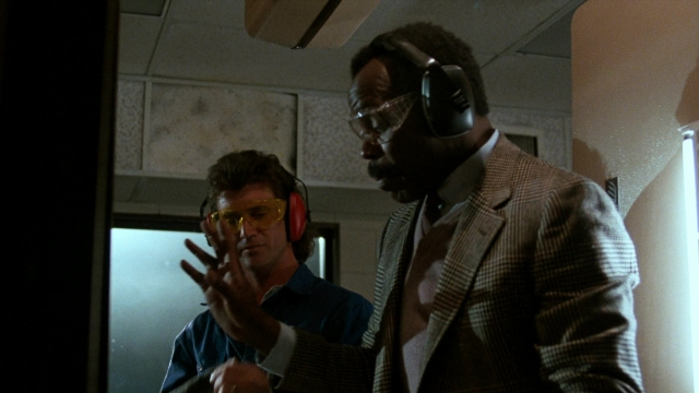 Wide shot frame from Lethal Weapon — room, dialogue, hand