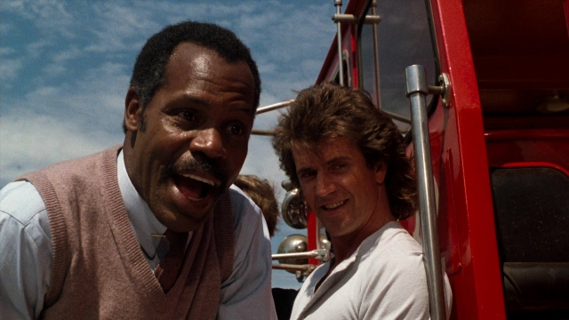 Wide shot frame from Lethal Weapon — sitting, standing, door