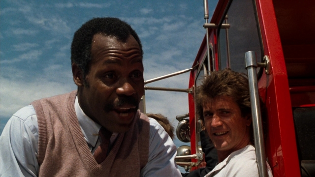 Wide shot frame from Lethal Weapon — sitting, dialogue, fire