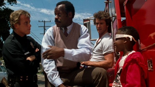 Medium shot frame from Lethal Weapon — sitting, street, uniform