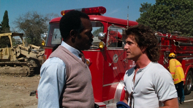 Wide shot frame from Lethal Weapon — standing, dialogue, fire