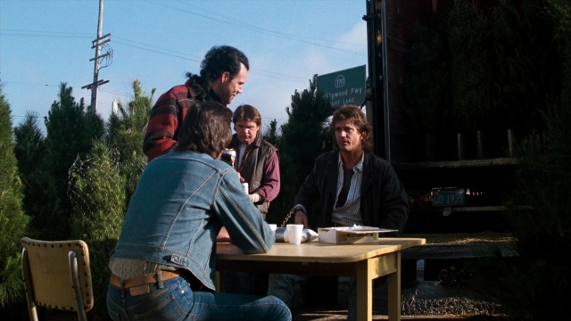 Wide shot frame from Lethal Weapon — sitting, standing, table