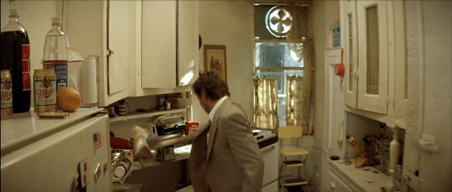 Wide shot frame from Léon — standing, kitchen, hand
