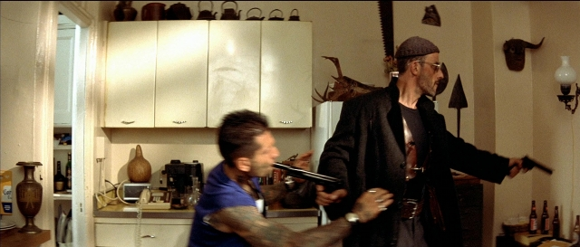 Wide shot frame from Léon — standing, hat, kitchen