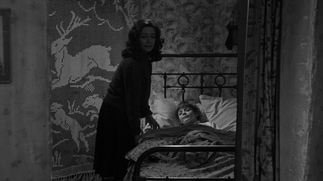 Wide shot frame from Léon Morin, prêtre — standing, room, bed
