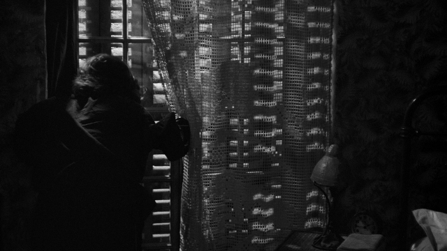 Wide shot frame from Léon Morin, prêtre — standing, room, bed
