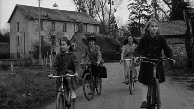 Wide shot frame from Léon Morin, prêtre — street, house, bicycle