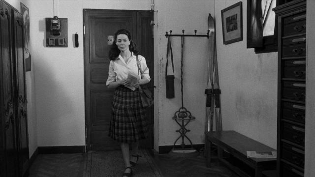 Wide shot frame from Léon Morin, prêtre — book, standing, phone